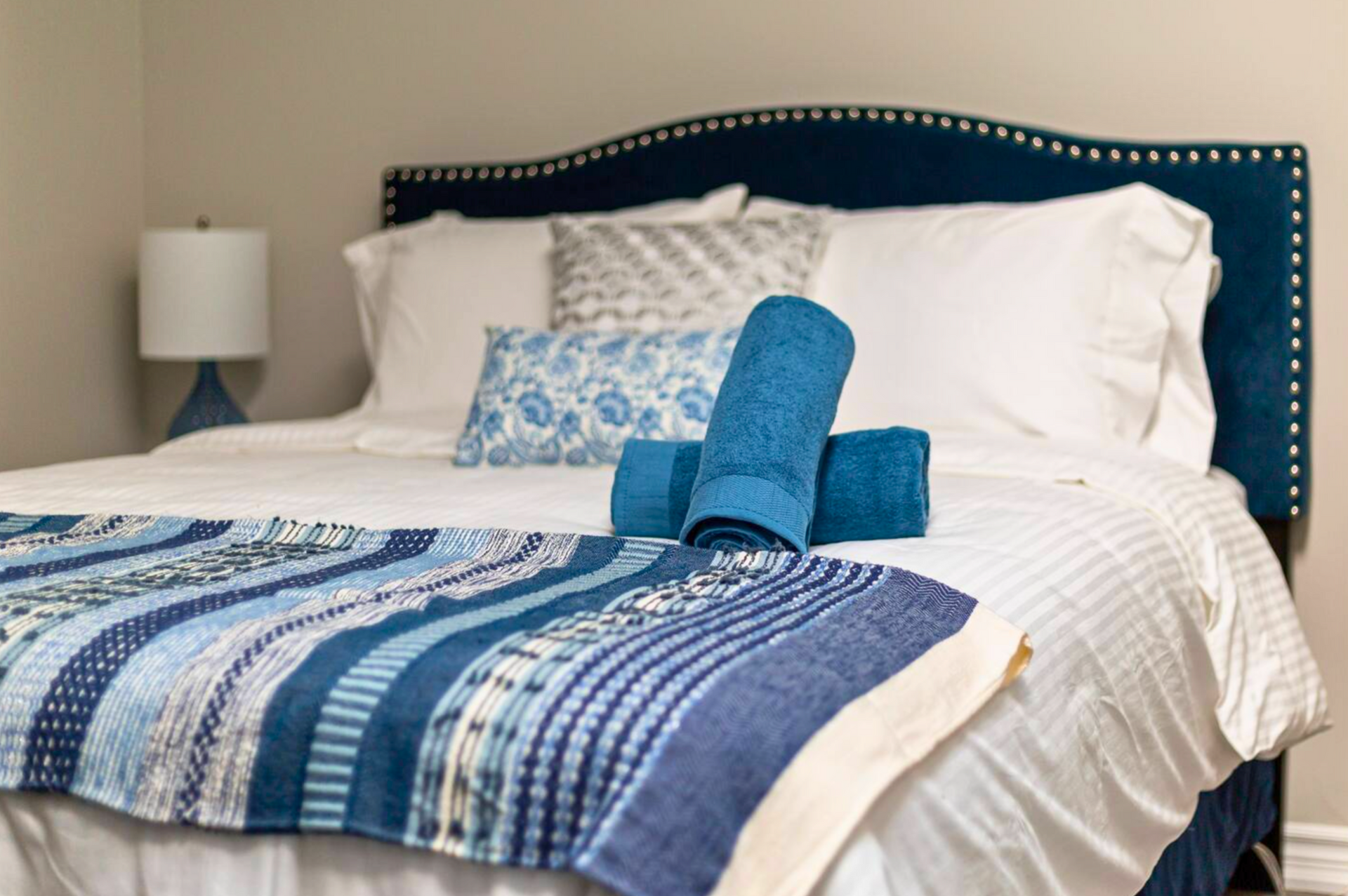 Bedroom with blue accents: bed with white bedding, blue headboard, towels, and patterned throw.