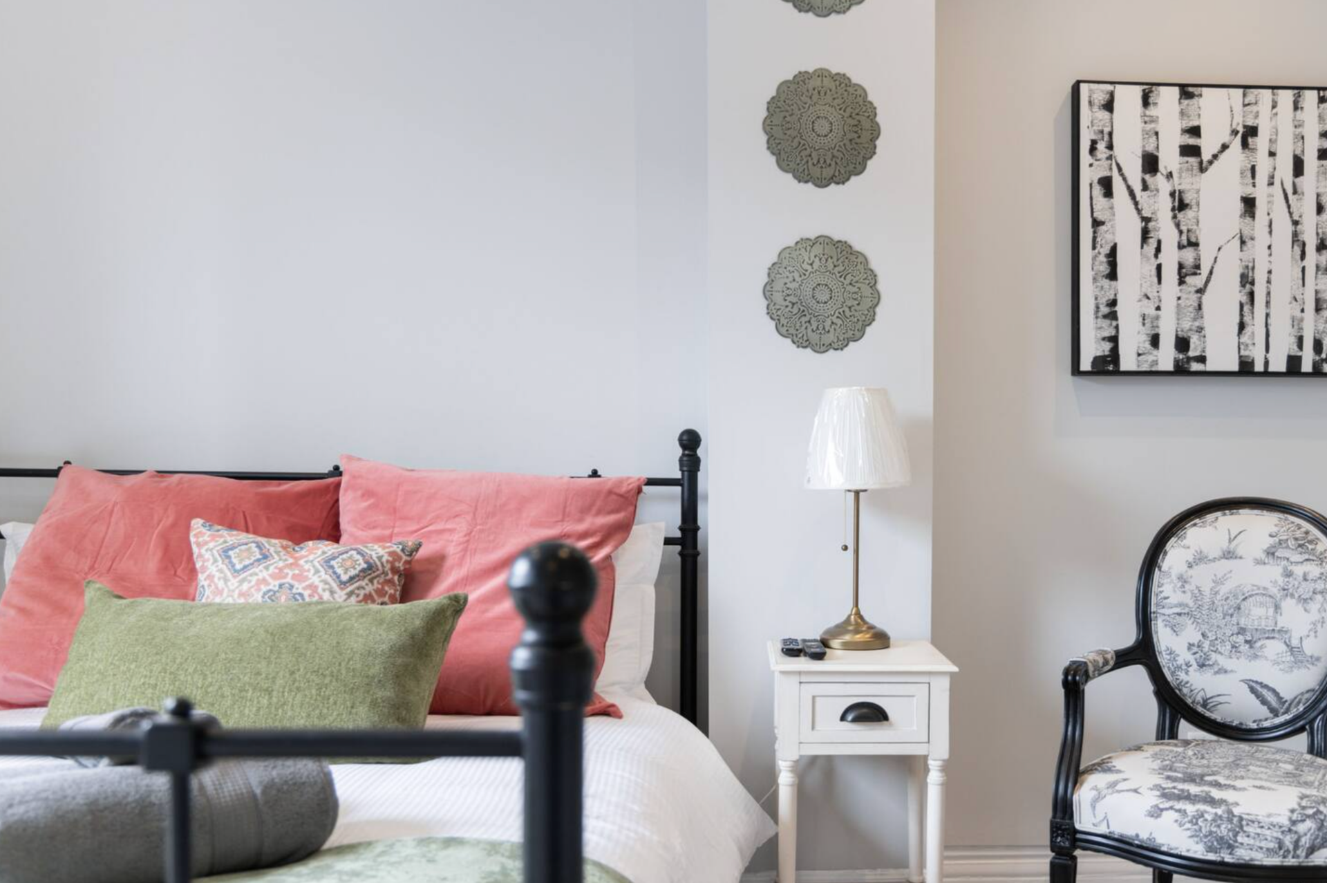 Bedroom corner with a black bed frame, a white nightstand with a lamp, and decorative wall art.