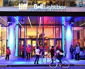 Entrance to the TIFF Bell Lightbox with neon lights and people entering, a person on a bicycle, and event staff.
