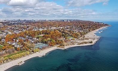 Aerial view of beach, park, and city skyline under a cloudy sky, with fall foliage in shades of orange and brown.