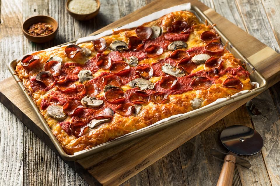 Square pizza with pepperoni and mushrooms on a baking sheet, wooden boards, spices.