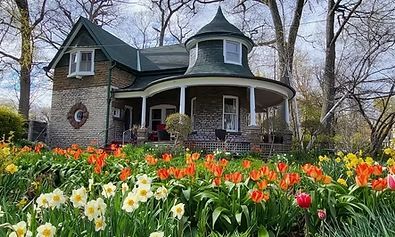 House with a curved porch and turret, surrounded by a garden of orange and yellow tulips and daffodils.