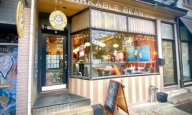 Coffee shop exterior with a striped awning, large windows, and a chalkboard sign.