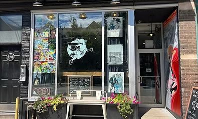 Storefront with large windows displaying art, open door, and flower boxes.