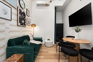 Small, stylish living room with a green velvet sofa, art, and a round dining table.