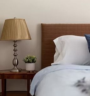Bedroom with lamp on a nightstand beside a bed with white sheets and a brown headboard.