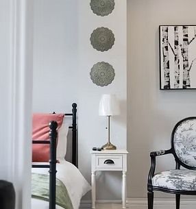 Bedroom with white nightstand, black iron bed, chair, and artwork. Decorative plates hang on the wall.