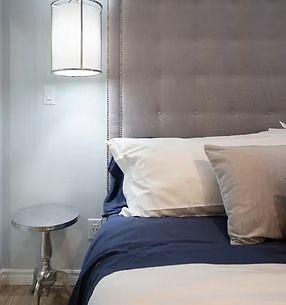 Bedroom corner: bed with blue blanket, white sheets, gray headboard, side table, pendant lamp.