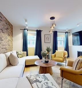 Living room with brick wall, white sofa, blue curtains, gold chairs, and a round wooden coffee table.