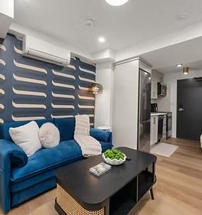 Blue sofa in a modern apartment living room with patterned accent wall, black coffee table, and kitchenette.