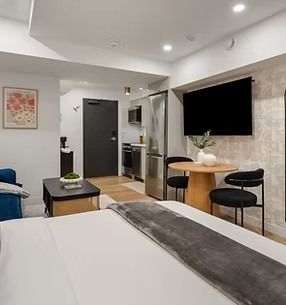Studio apartment interior with bed, small dining table, TV, and kitchenette.