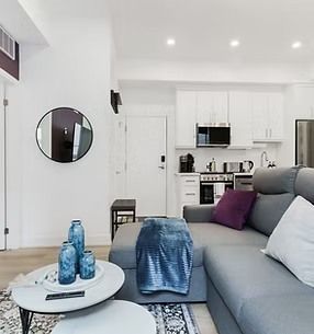 Living room with gray sectional sofa, white walls, and kitchen in the background.