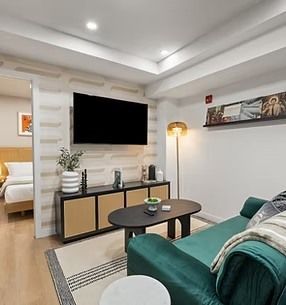 Living room with a teal sofa, TV, and coffee table. Bedroom visible through doorway.
