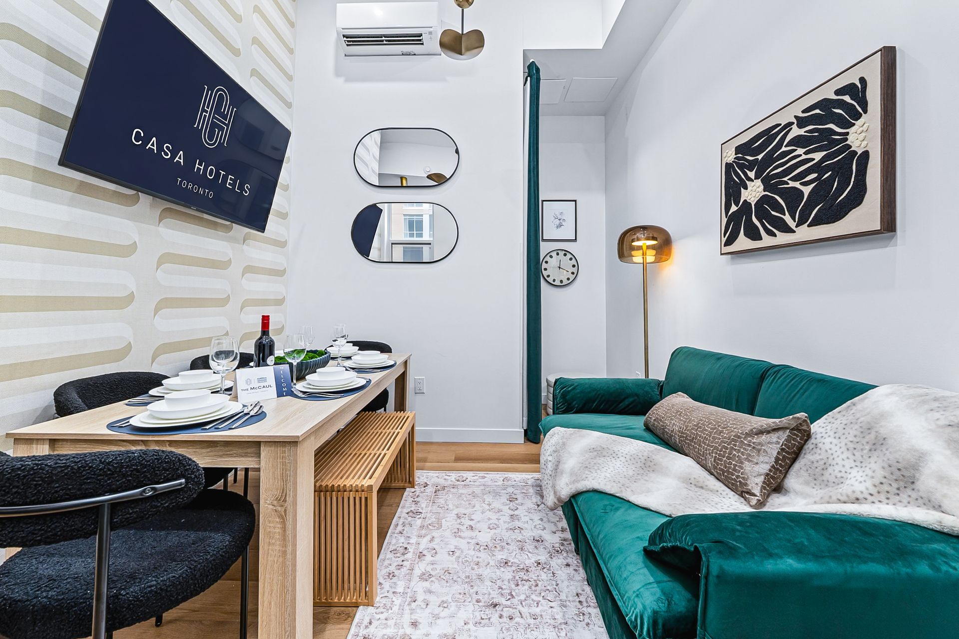 Small modern living room with teal sofa, wall art, dining table, and white rug