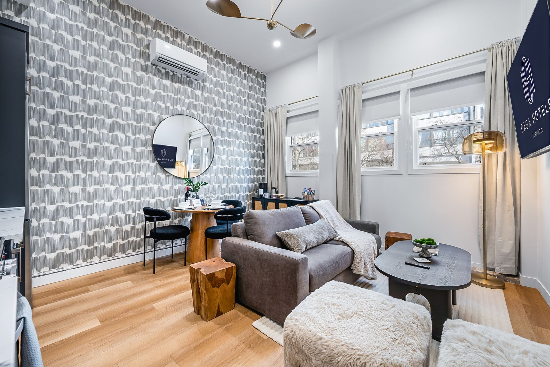 Bright modern living room with gray sofa, patterned accent wall, round mirror, and large windows