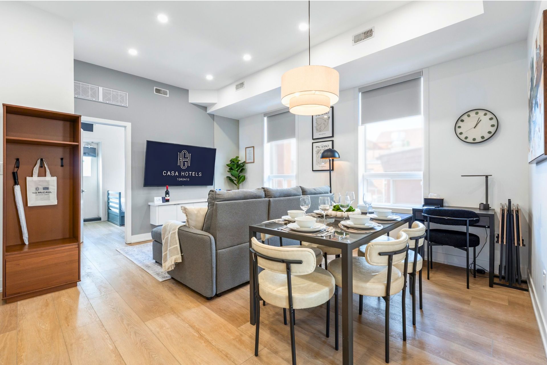 Bright open living-dining room with gray sofa, round table, wooden floor, and large windows