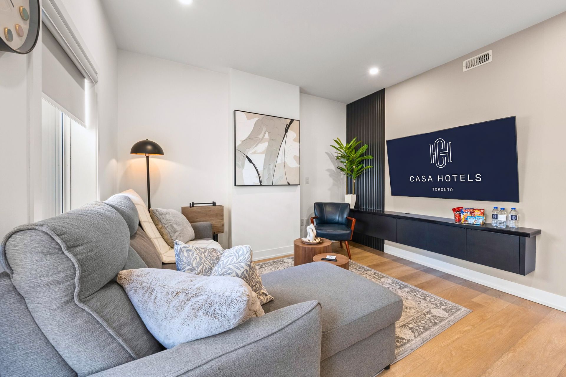Bright modern living room with gray sofa, floor lamp, wall art, and wall-mounted TV