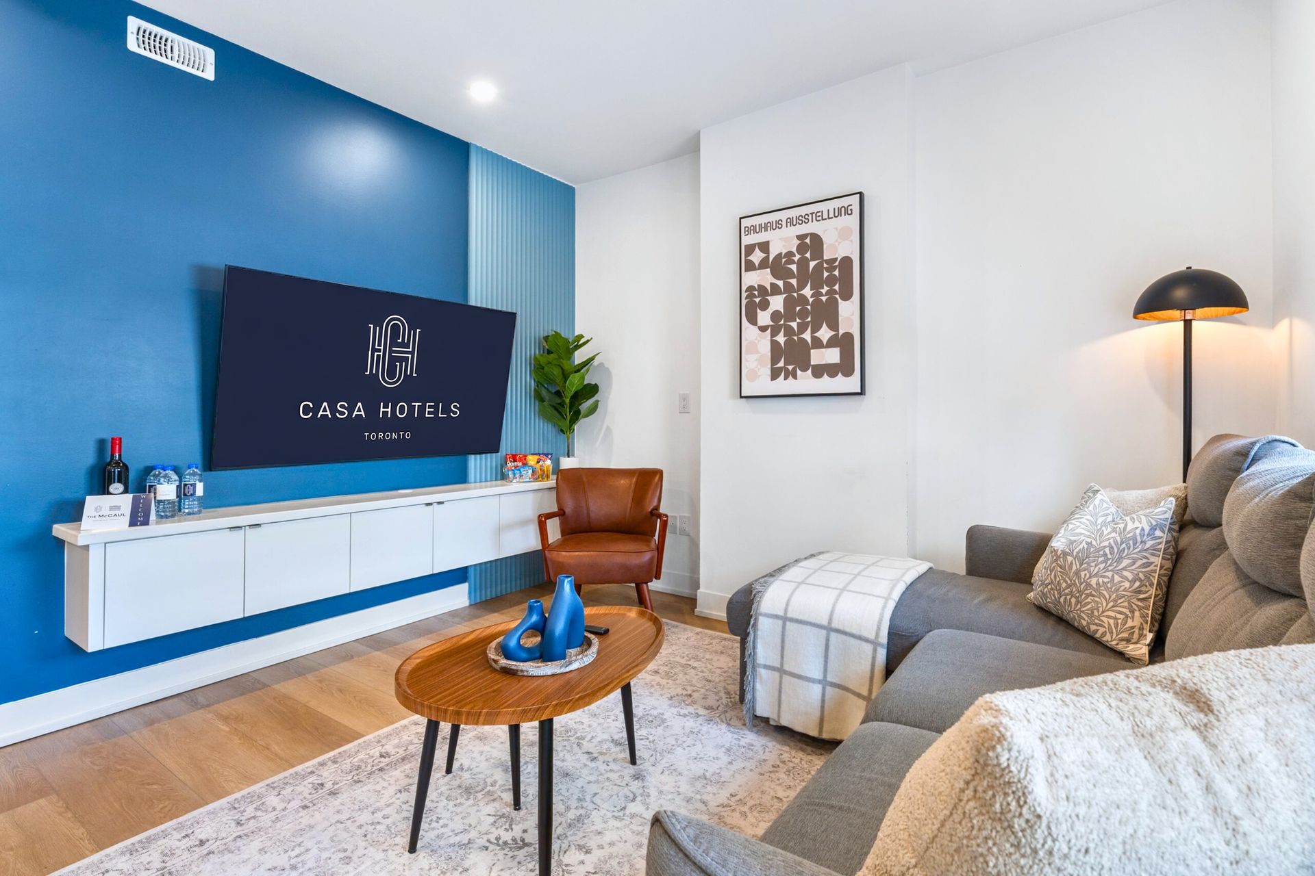 Bright living room with blue accent wall, wall-mounted TV, gray sofa, and wooden coffee table
