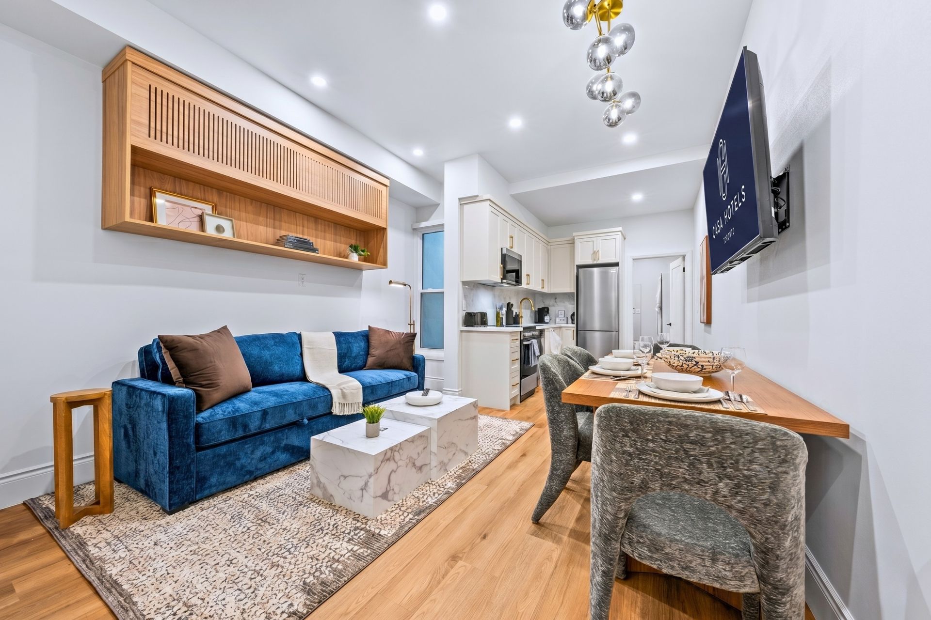 Bright modern living-dining room with blue sofa, wooden table, and compact kitchen in the background