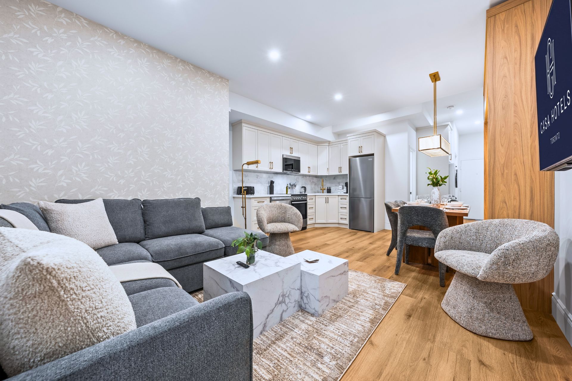 Bright living room with gray sofa, white coffee tables, dining nook, and open kitchen with wood floors