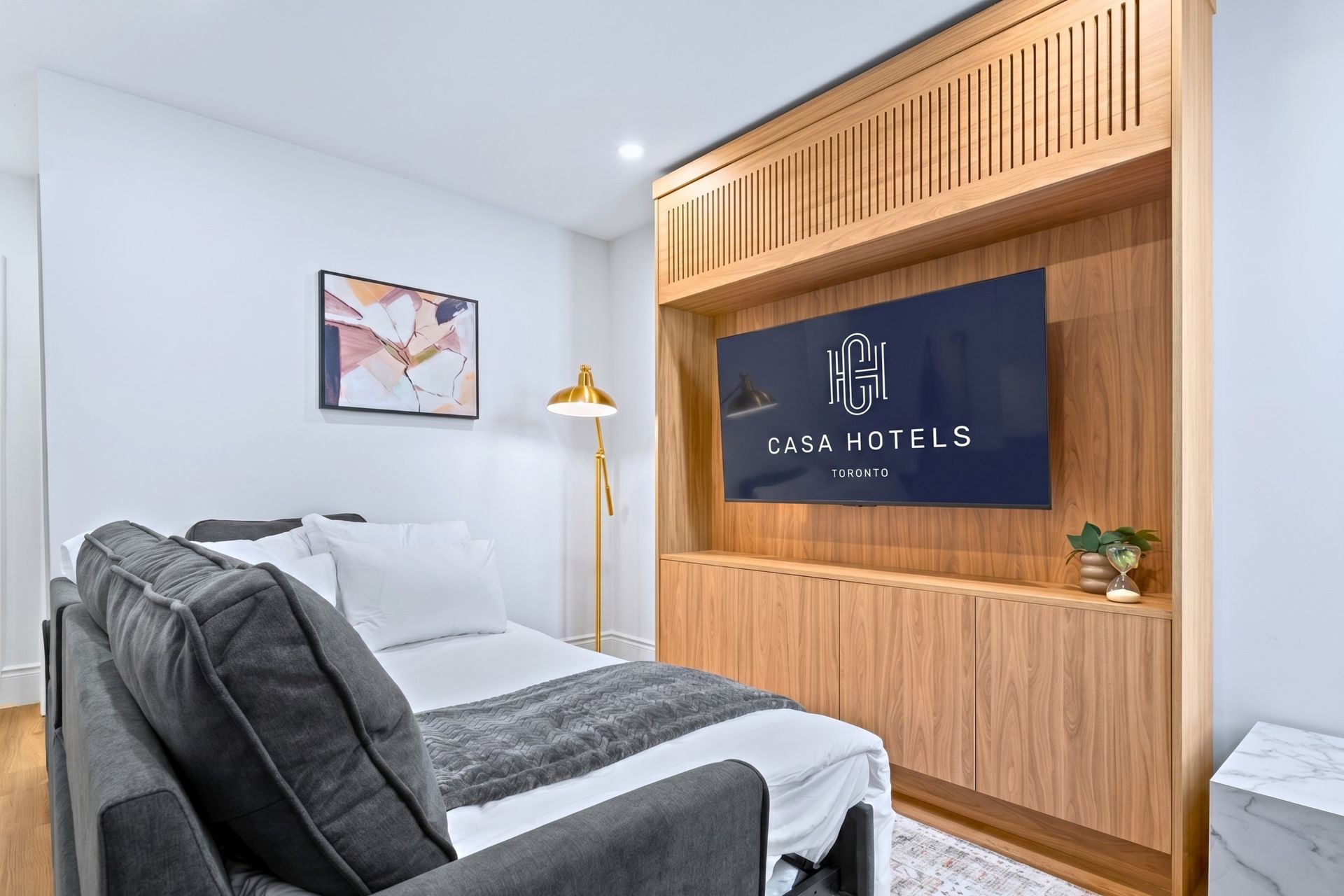 Modern bedroom with a gray sofa, wooden TV wall, and wall-mounted television