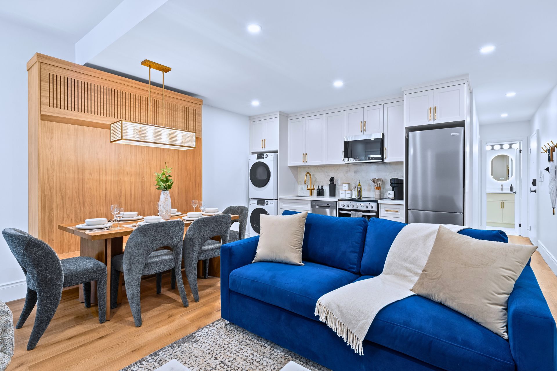 Bright open-plan living room with blue sofa, dining table, and white kitchen cabinets