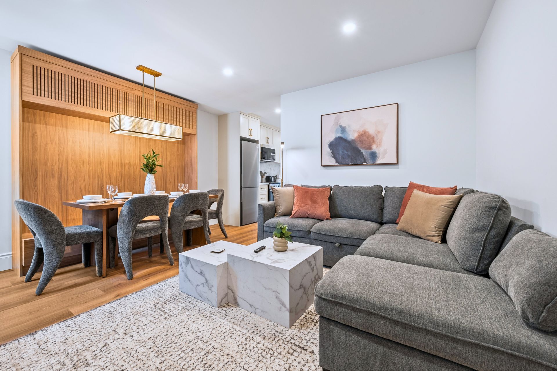 Modern living-dining room with gray sectional, wooden dining table, and open kitchen design