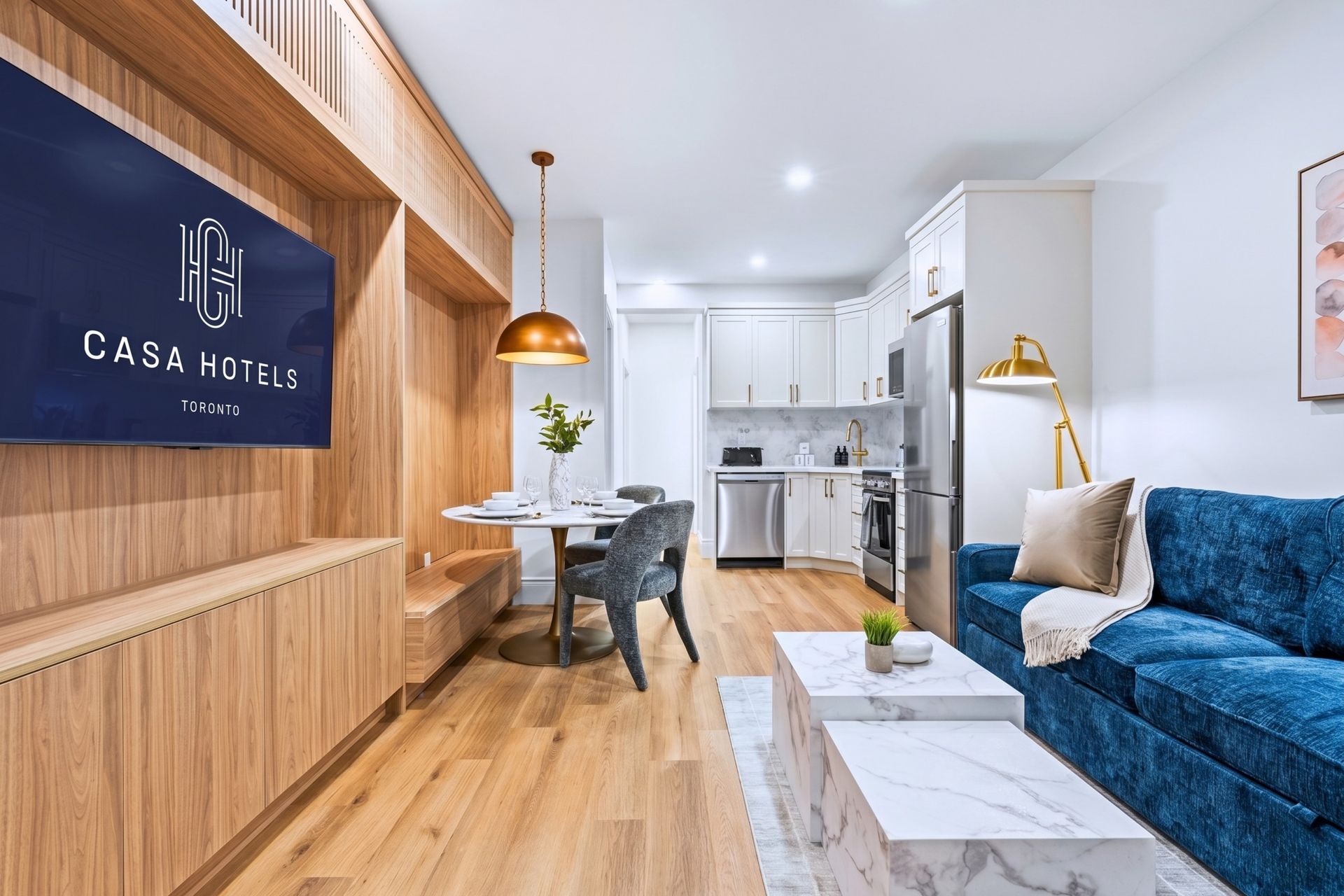 Bright open-concept living room with blue sofa, wood accent wall, dining table, and white kitchen.