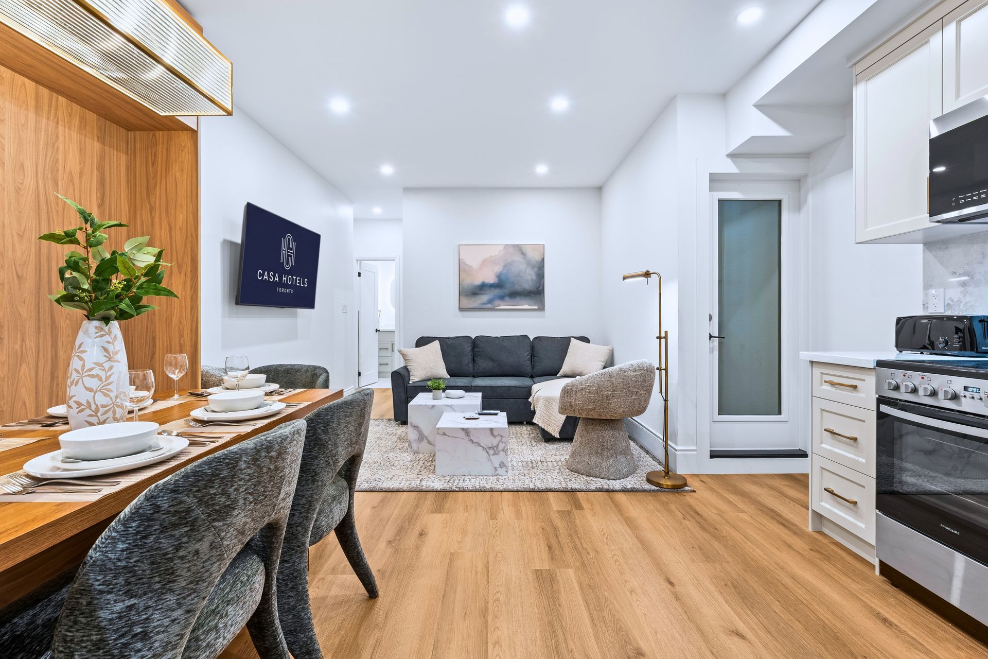Modern open-plan living room and kitchen with wood floors, gray sofa, dining table, and white cabinets