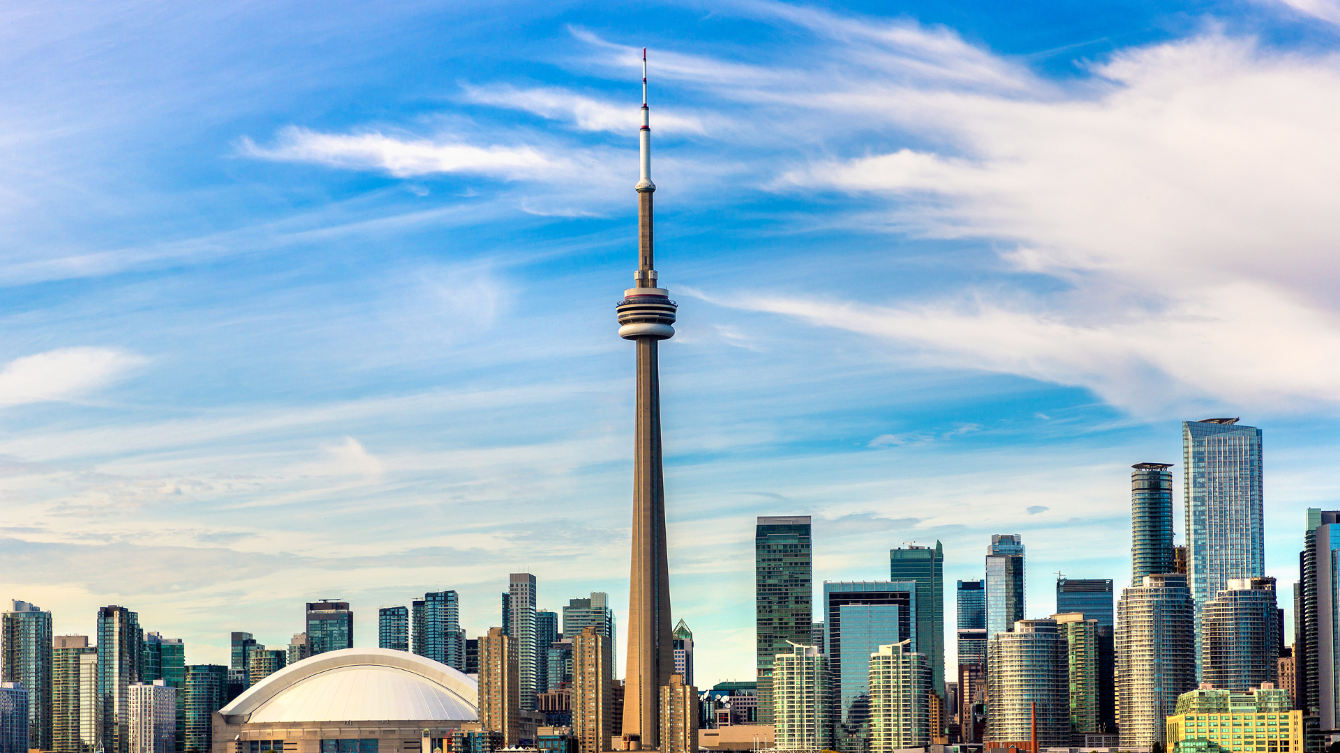 Toronto skyline with CN Tower and Rogers Centre under a blue, cloud-streaked sky