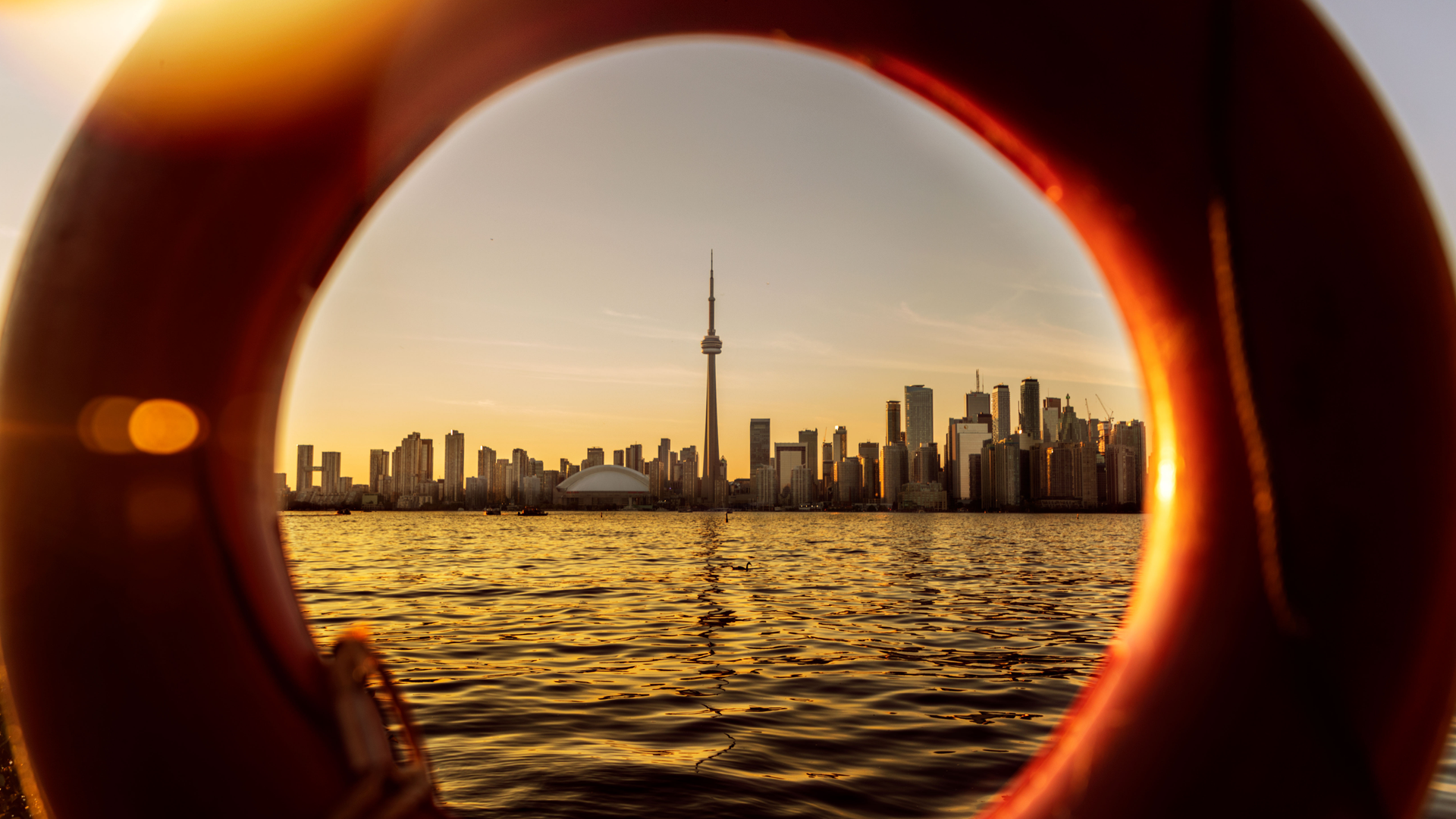 Sunset skyline across water, framed by a red circular opening with golden reflections on the waves