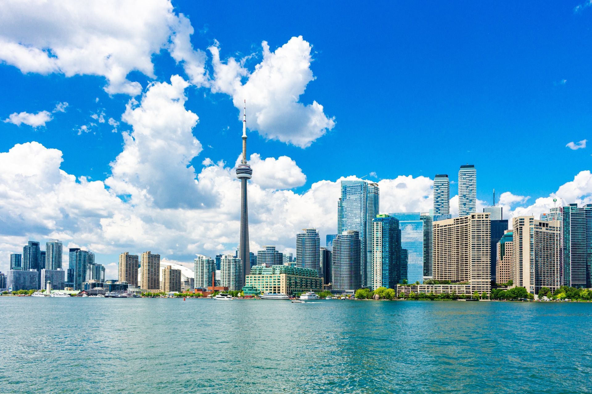 Toronto skyline with CN Tower under a bright blue sky above calm waterfront