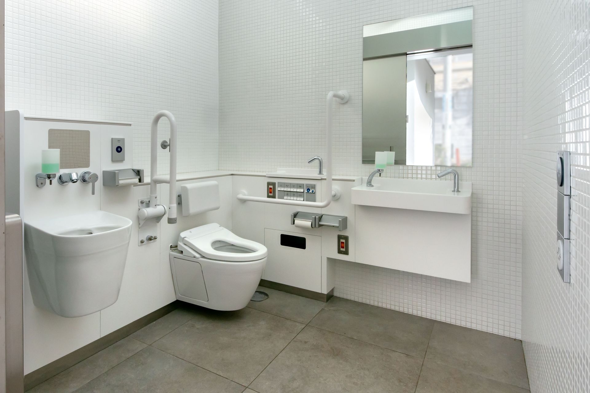 Salle de bain avec murs carrelés blancs, toilettes, lavabo et barres d'appui.