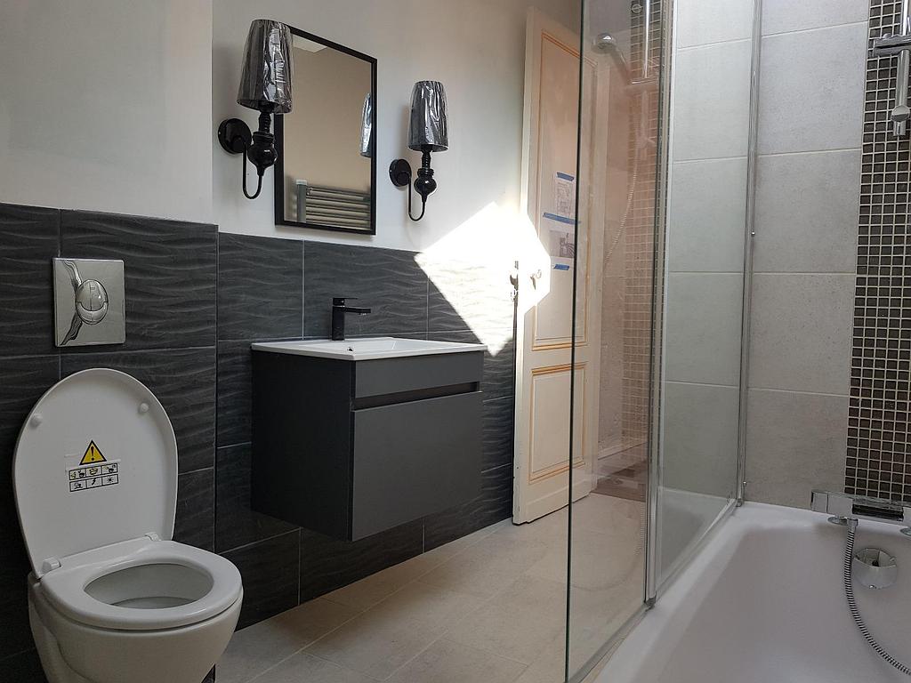 Salle de bain avec WC, lavabo, miroir et douche, avec une décoration noire et grise.