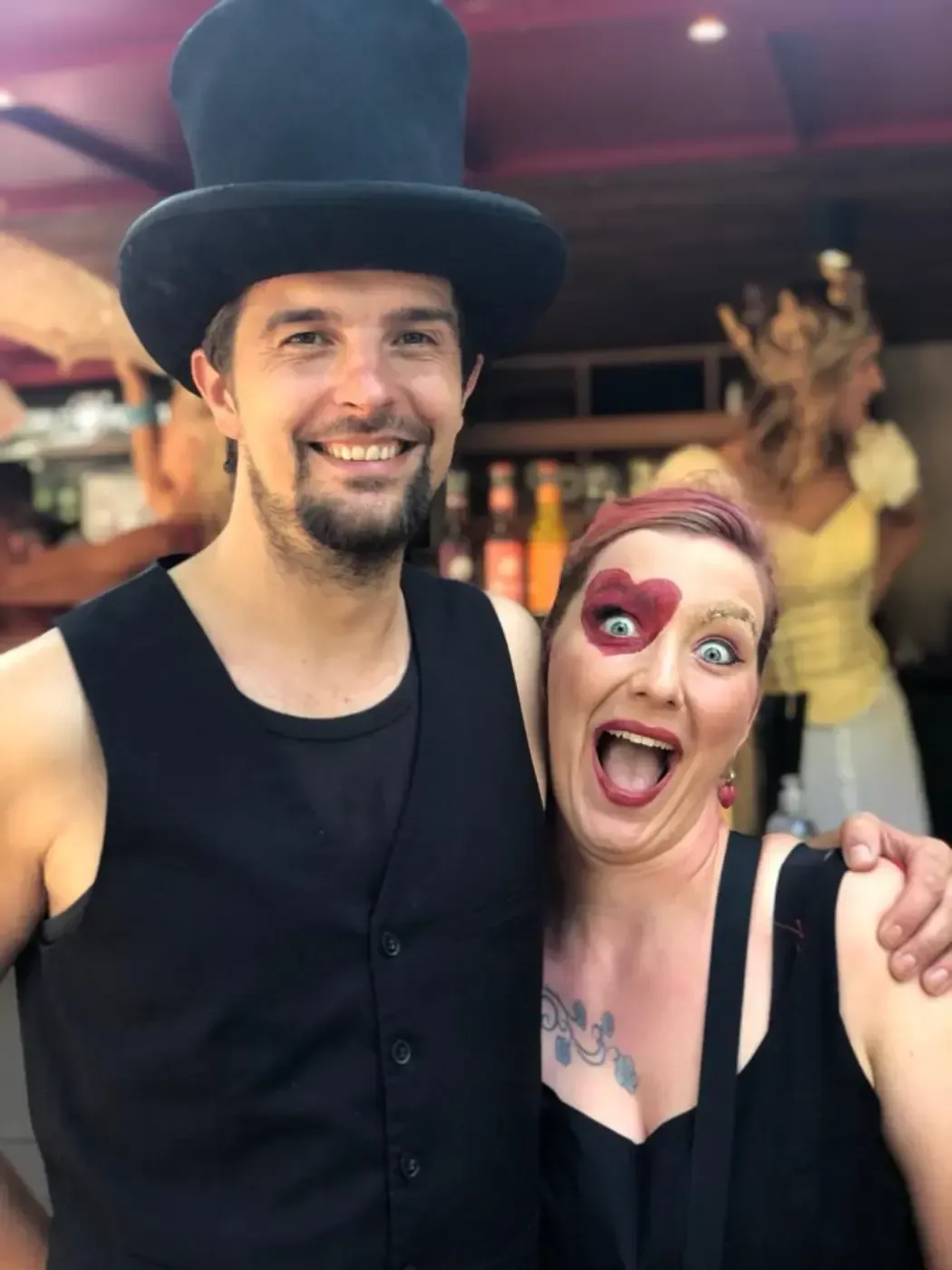 Ein Mann mit Zylinder steht neben einer Frau mit roter Farbe im Gesicht.