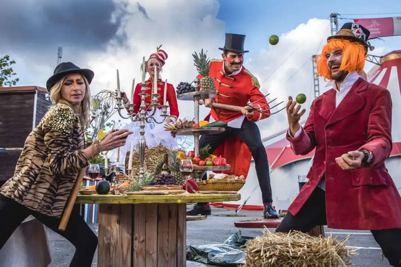 Eine Gruppe von Menschen in Zirkuskostümen steht um einen Tisch herum.