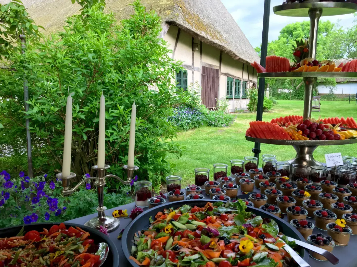 Ein Buffettisch mit Essen und Kerzen vor einem strohgedeckten Gebäude.