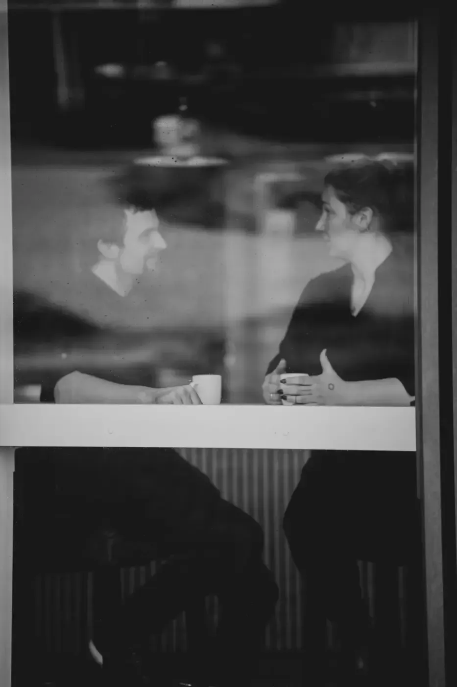 Ein Mann und eine Frau sitzen an einem Tisch vor einem Fenster und trinken Kaffee.