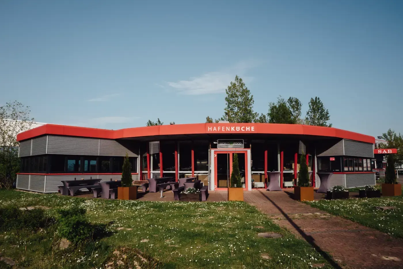 Ein großes Gebäude mit einem roten Dach ist von Gras und Bäumen umgeben.