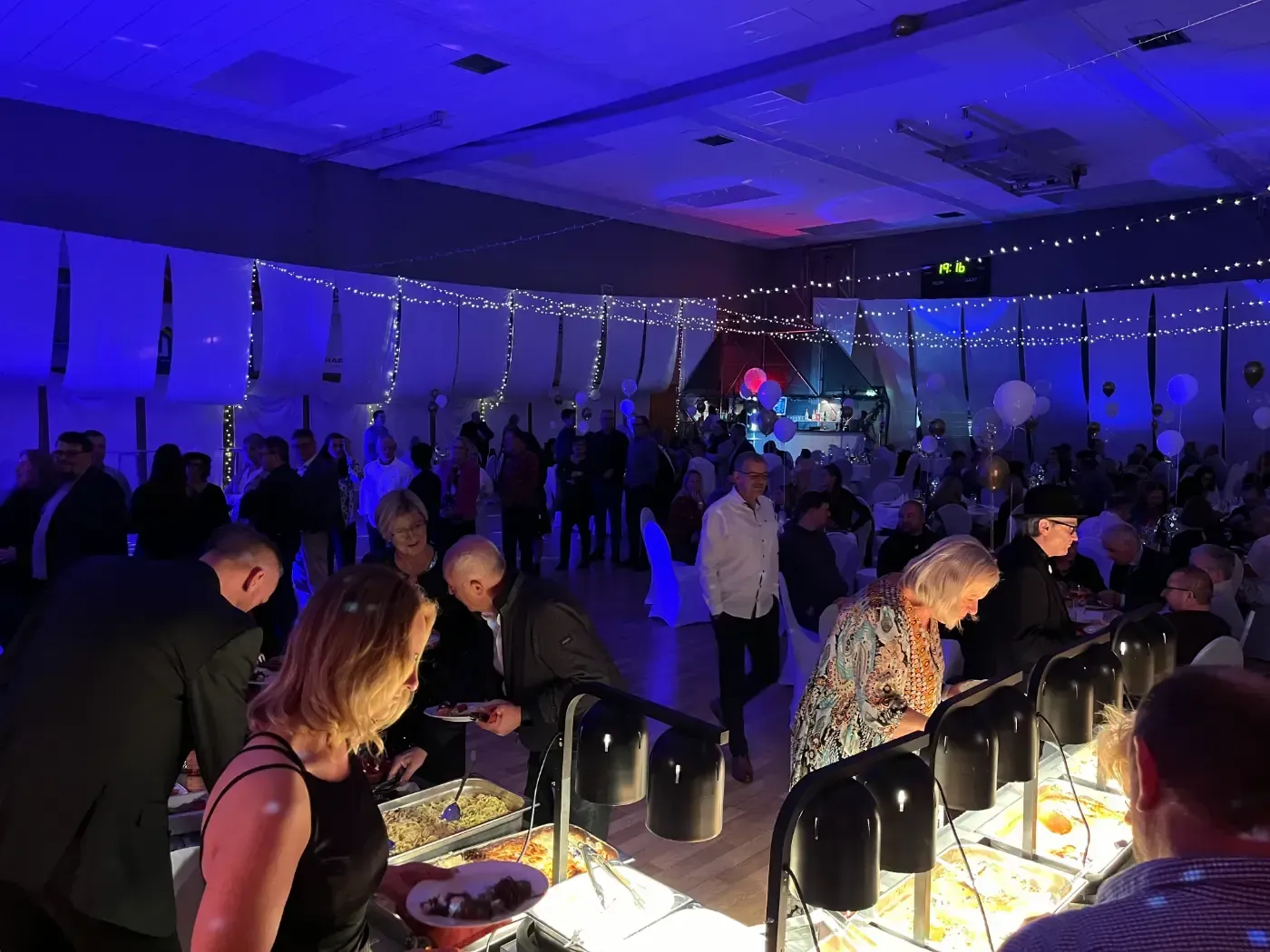 Eine große Gruppe von Menschen steht bei einer Party um ein Buffet herum.