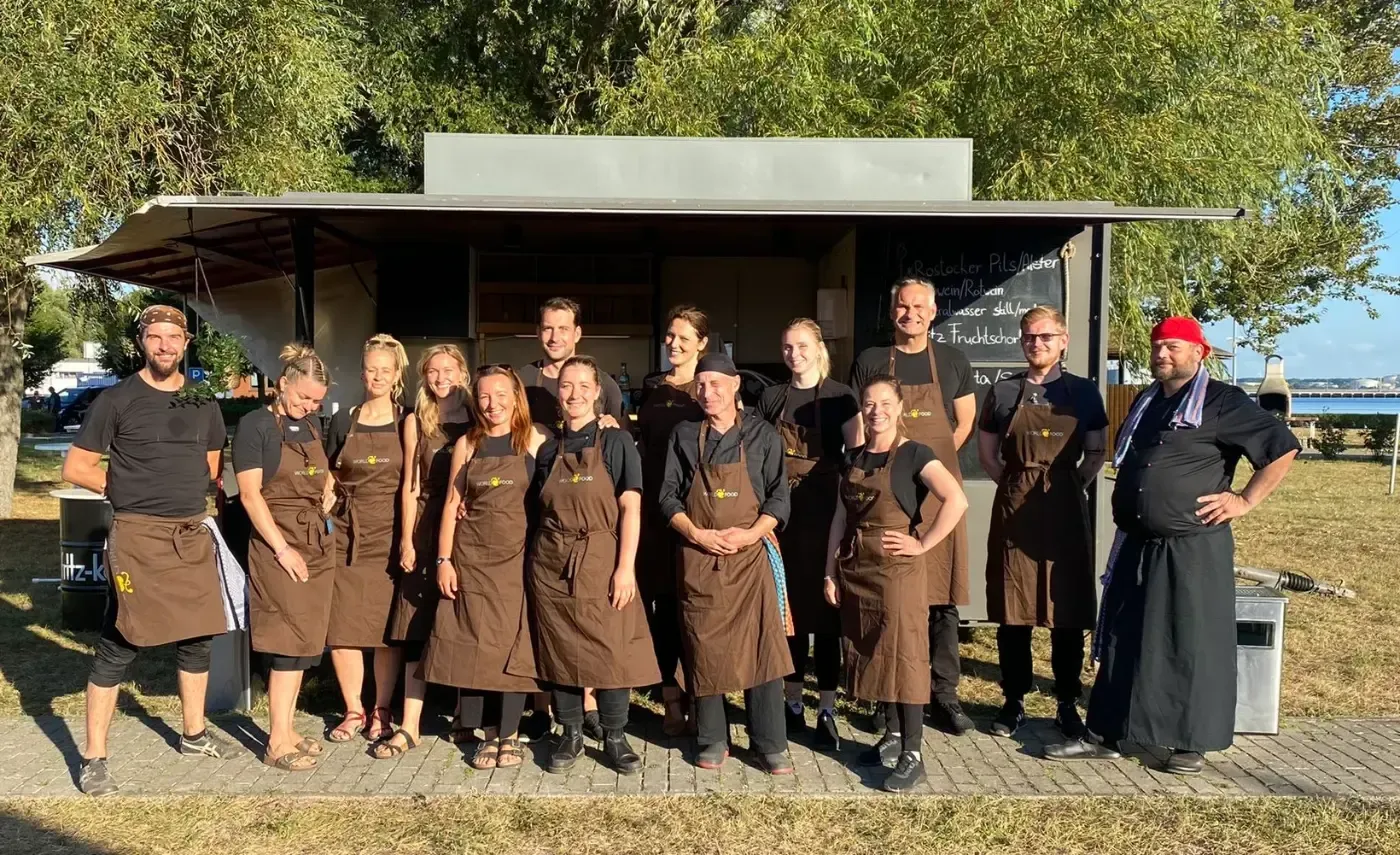 Eine Gruppe von Menschen in Schürzen posiert vor einem Imbisswagen für ein Foto.