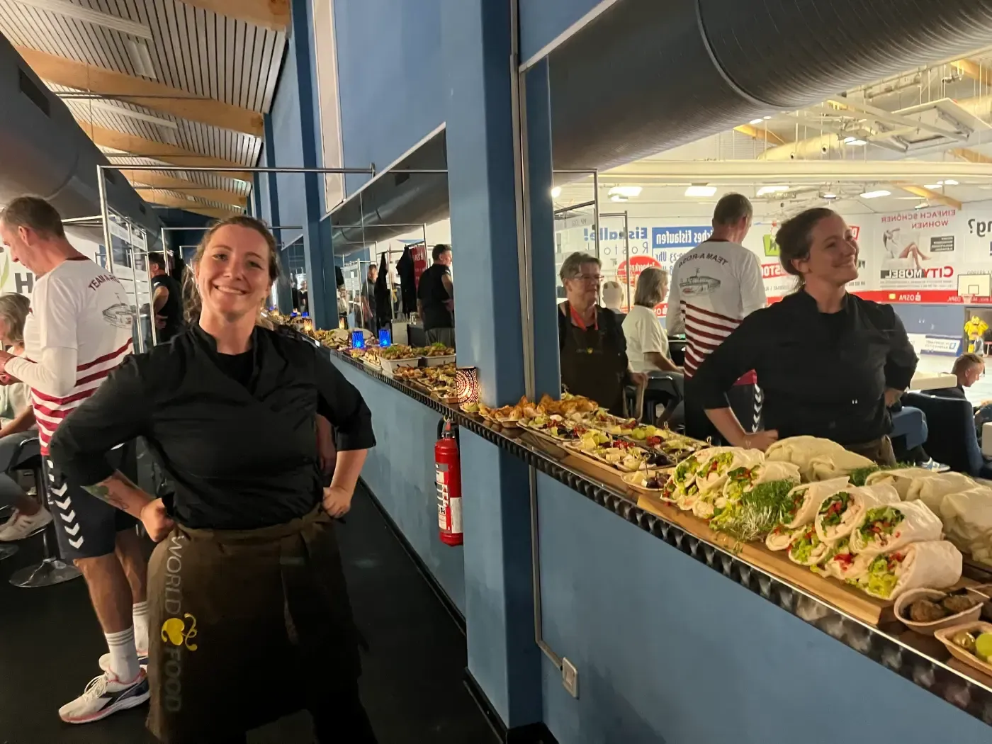 Eine Frau steht vor einem langen Tablett mit Essen.