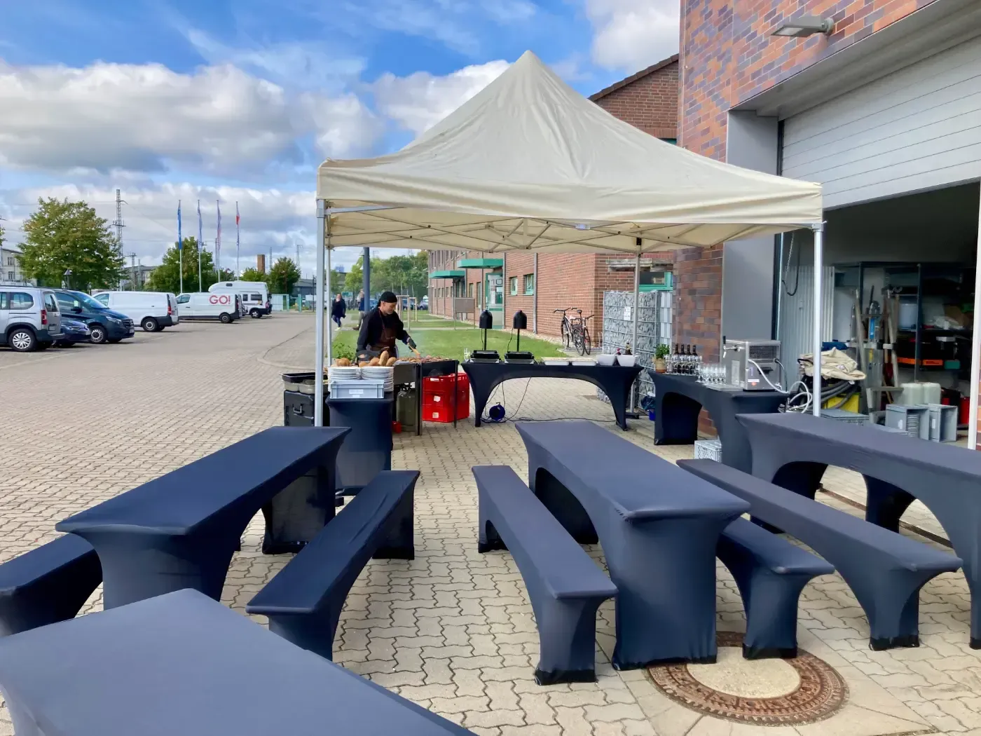 Eine Gruppe von Tischen und Bänken unter einem Zelt auf einem Parkplatz.