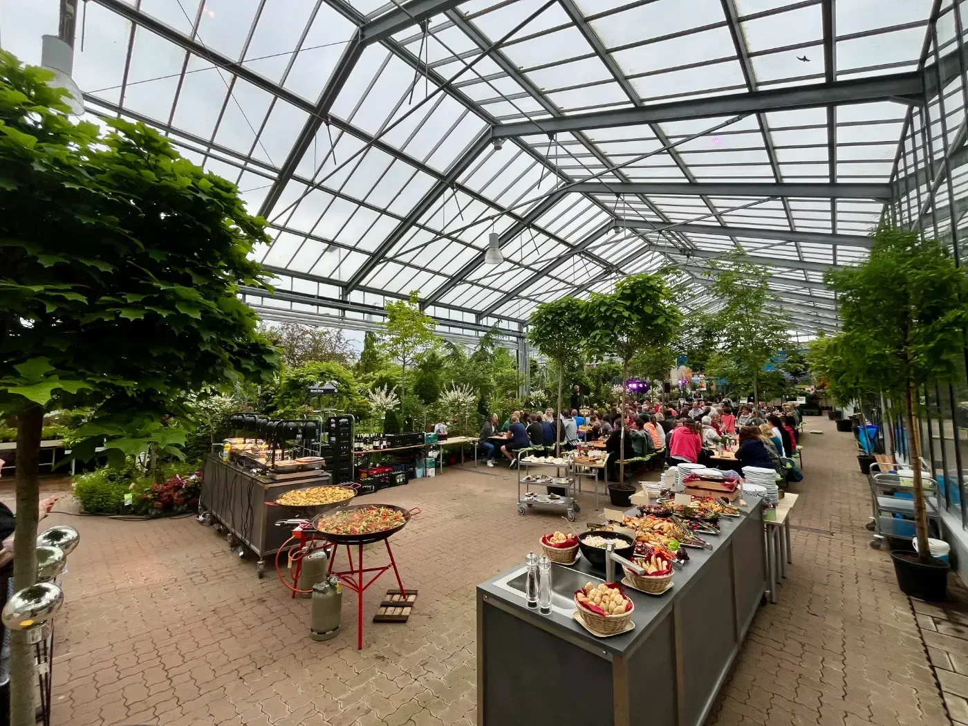 Eine Gruppe von Menschen sitzt an Tischen in einem Gewächshaus.