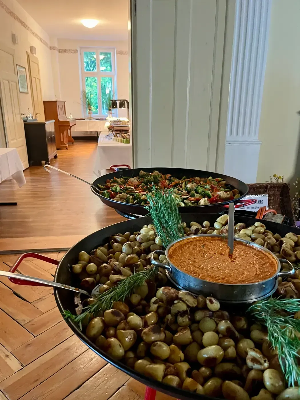 Zwei Pfannen mit Essen stehen auf einem Holztisch in einem Raum.
