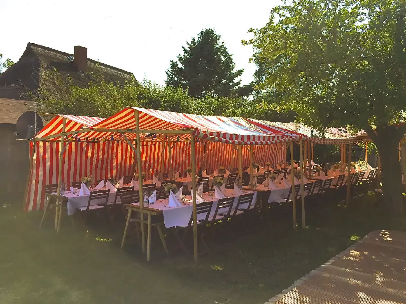 Eine Reihe von Tischen und Stühlen unter gestreiften Zelten in einem Garten.