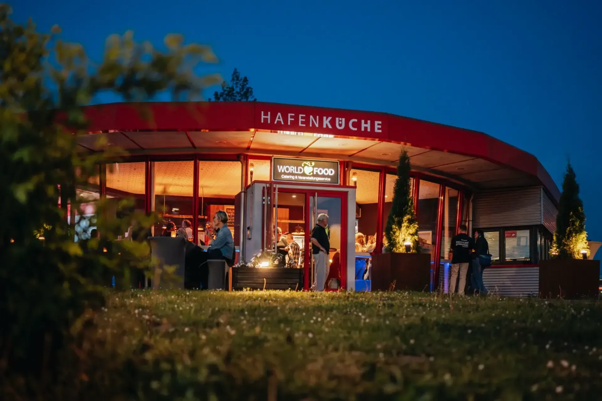 Eine Gruppe von Menschen steht nachts vor einem Restaurant.