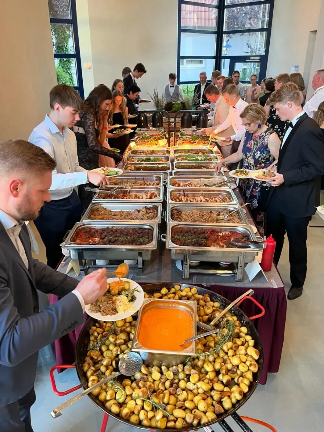 Eine Gruppe von Menschen steht um einen Buffettisch herum und isst.