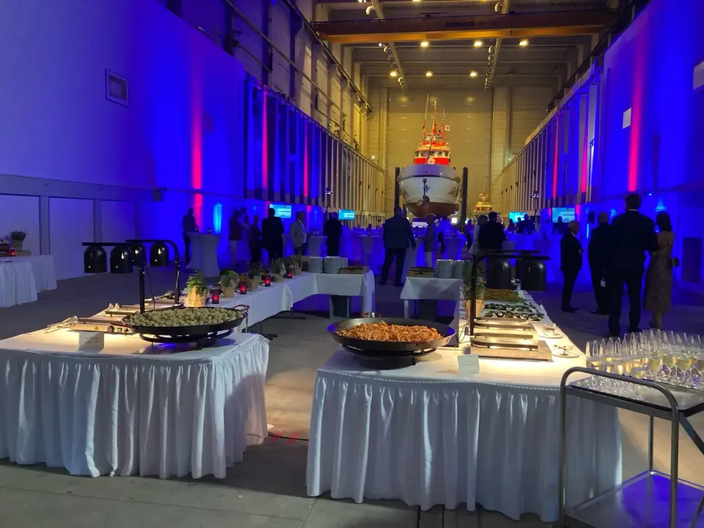 Ein großer Raum mit vielen Tischen und herumstehenden Leuten.