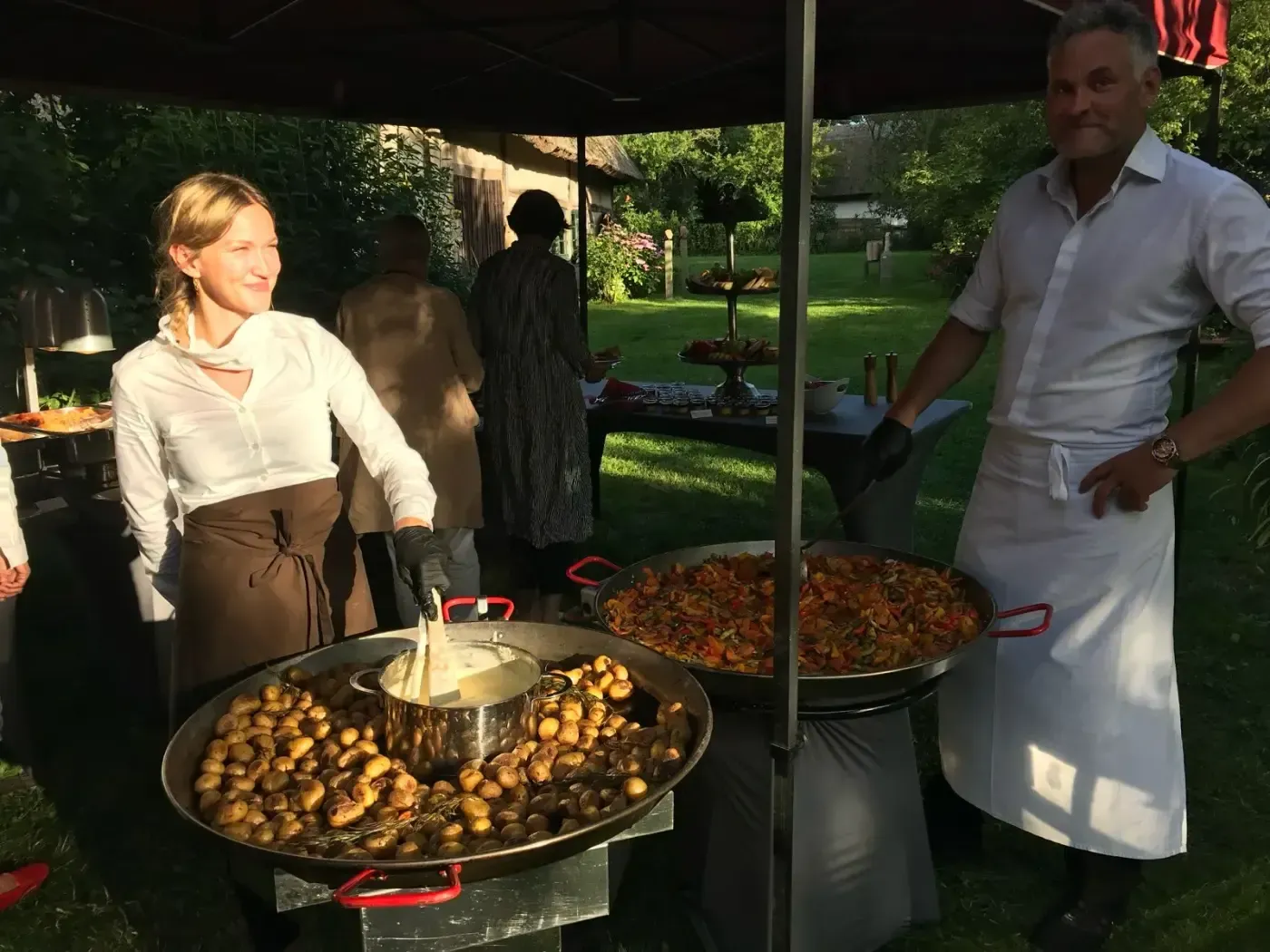 Ein Mann und eine Frau stehen vor Pfannen mit Essen.